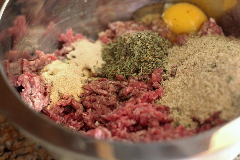 ground beef with breadcrumbs, egg and spices to make meatballs in a mixing bowl