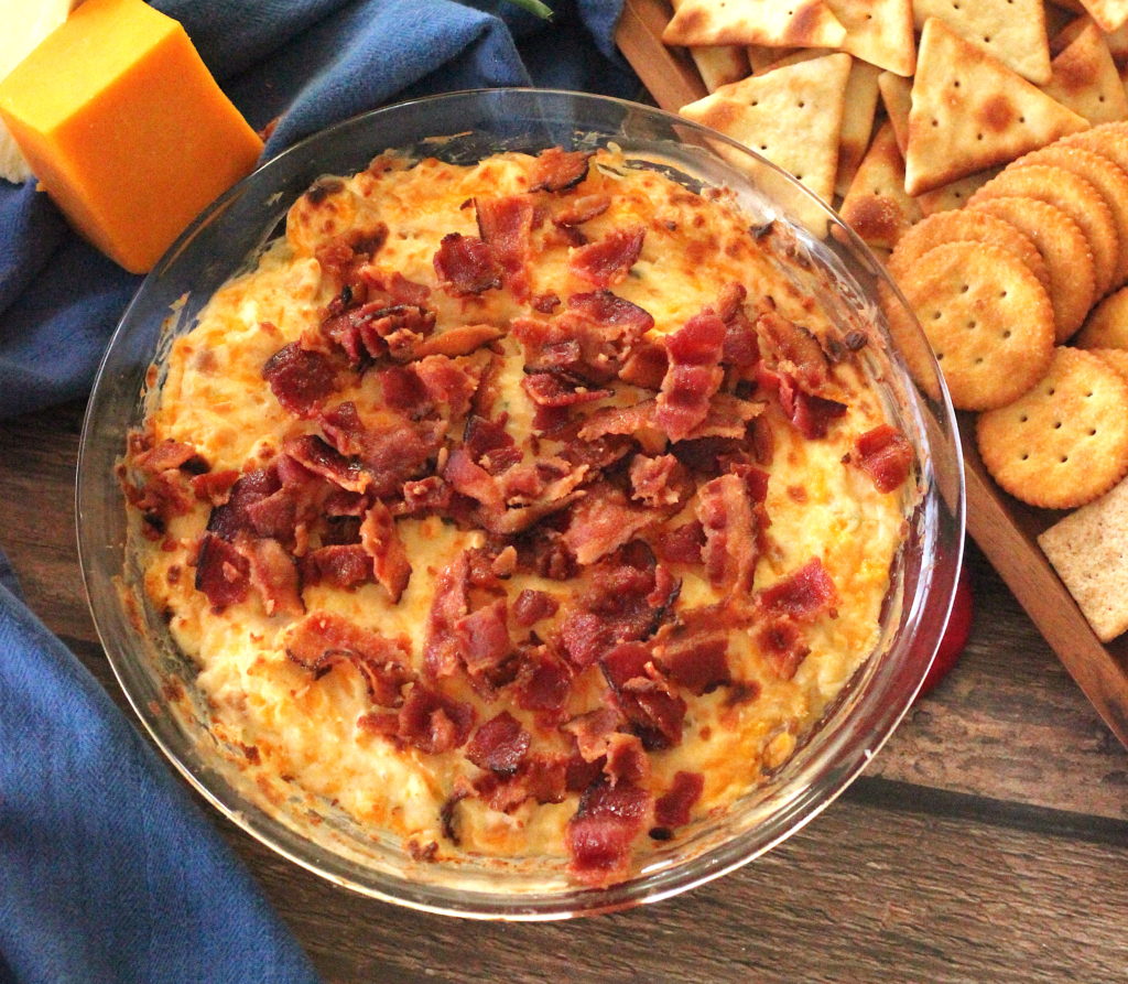 Image of a glass pie pan with hot cheddar cheese dip topped with crispy bacon. 