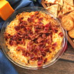 Image of a glass pie pan with hot cheddar cheese dip topped with crispy bacon.