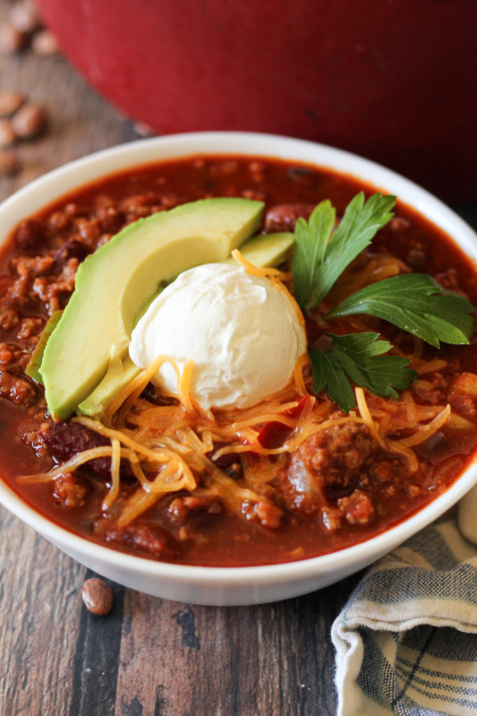 chili in a white bowl topped with avocado and sour cream
