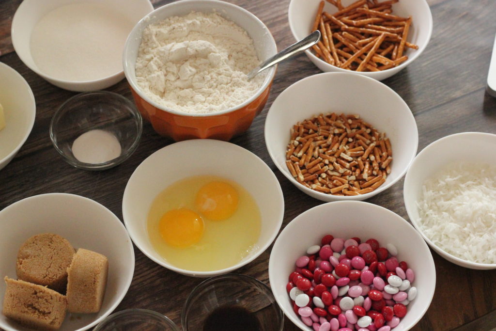 Ingredients for Coconut Chocolate Crunch Cookies. Picture of eggs, butter, flour, sugars, candies, pretzels and coconut. 