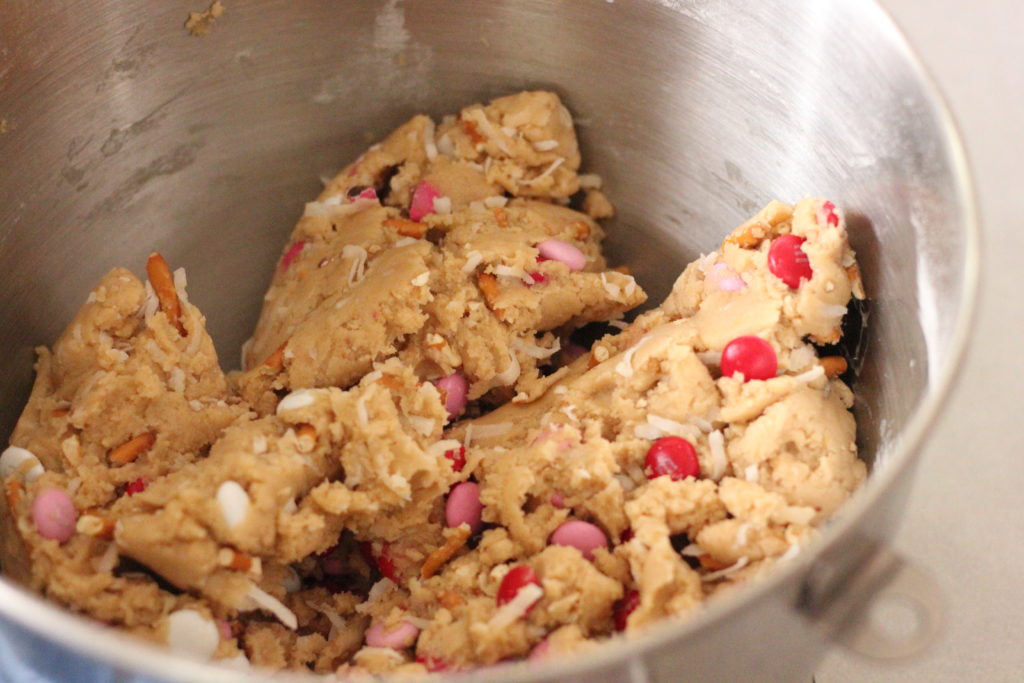 Image of coconut chocolate crunch cookie dough showing m & ms and coconut and pretzel pieces. 