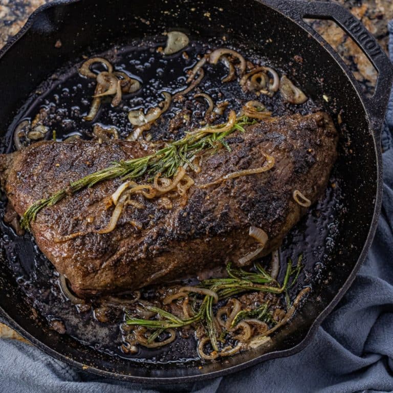 tri tip cooked in a cast iron pan topped with cooked shallots and rosemary