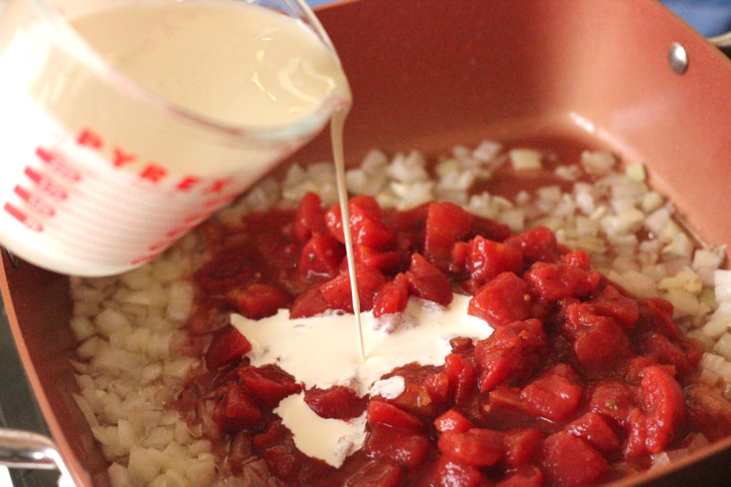 Cream pouring into a pan of onions and tomatoes