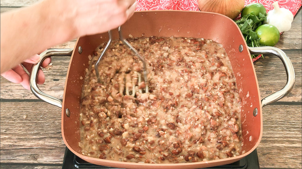 mashing refried beans with potato masher