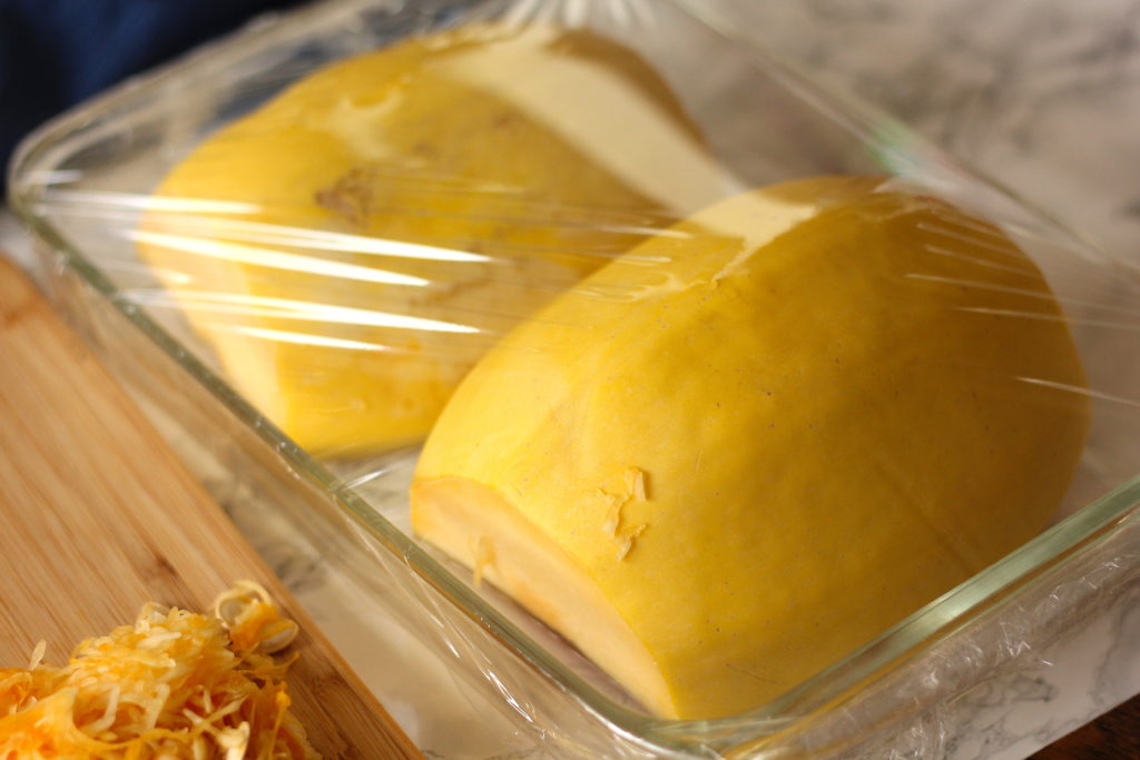 spaghetti squash in a baking dish covered with plastic wrap