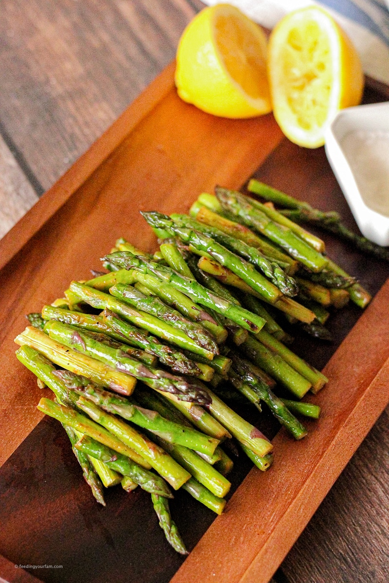 small stems of asparagus piled on a wooden platter with a side of lemon