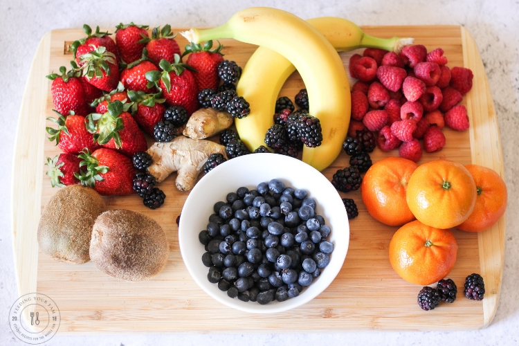 berries, bananas, oranges and kiwi on a cutting board