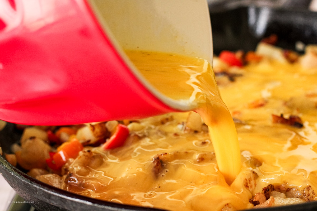 pouring eggs into a skillet with potatoes and bacon
