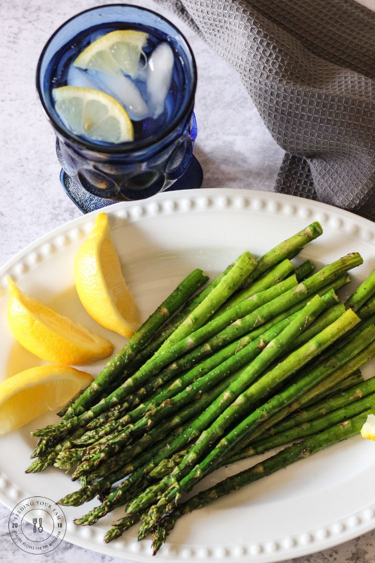 Grilled asparagus on a white plate with lemon wedges