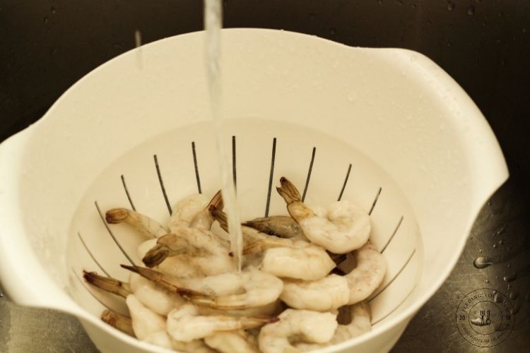 frozen shrimp in a colander with running water