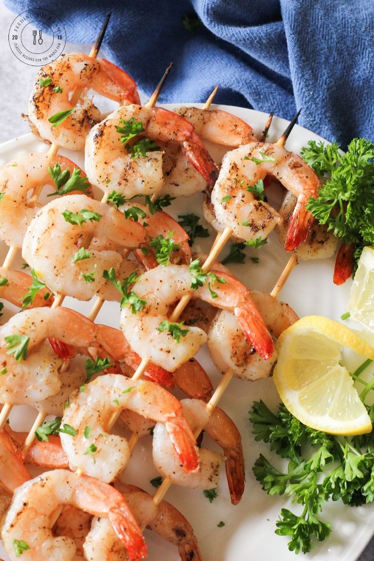 grilled shrimp skewers on a white plate with lemon and parsley