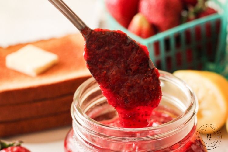spoon dripping strawberry jam into a jar