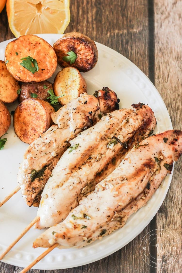 chicken kabobs on a white plate with potatoes