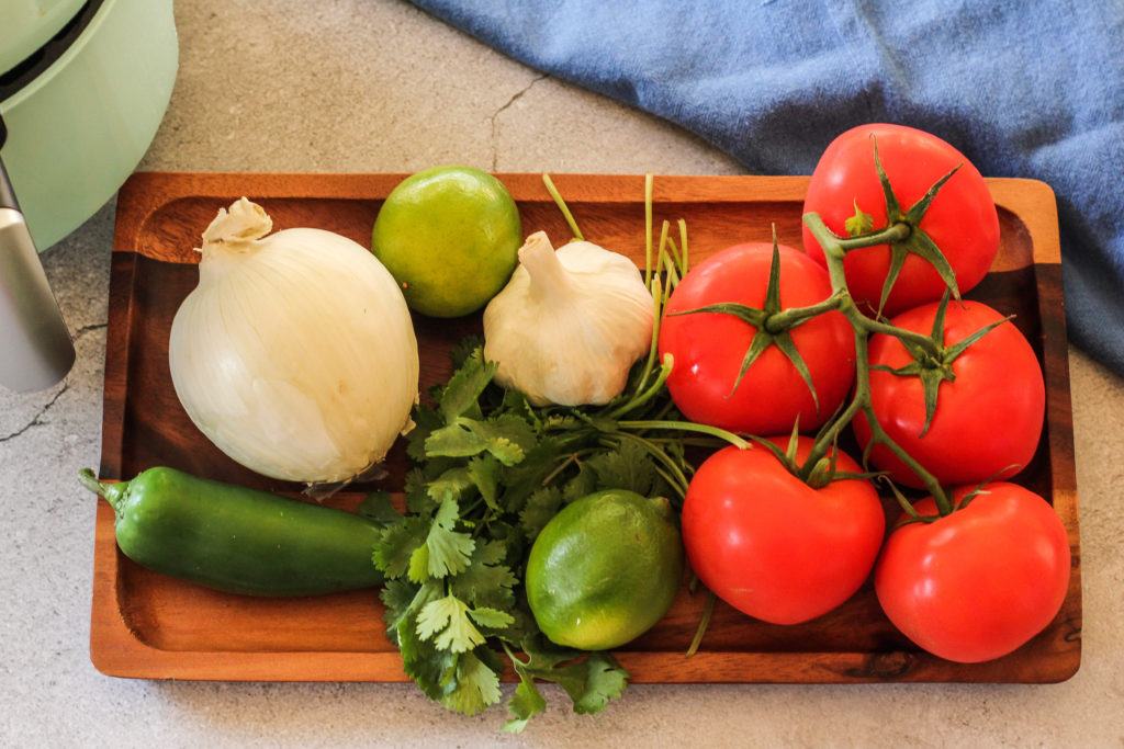 tomatoes, onion, garlic, limes, cilantro and jalapeno on a wooden platter