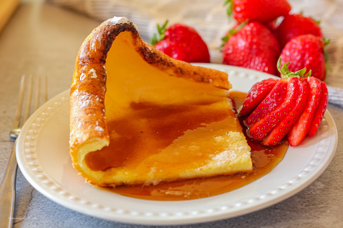 German Pancakes (also known as dutch baby pancakes) are a pan pancake that gets puffy and golden in the oven. This is a breakfast staple at our house! Easy to make, even the older kids can make this on their own! #germanpancakes #brunch #breakfast #dutchbaby #ovenpancake slice of puffy German pancake topped with maple syrup