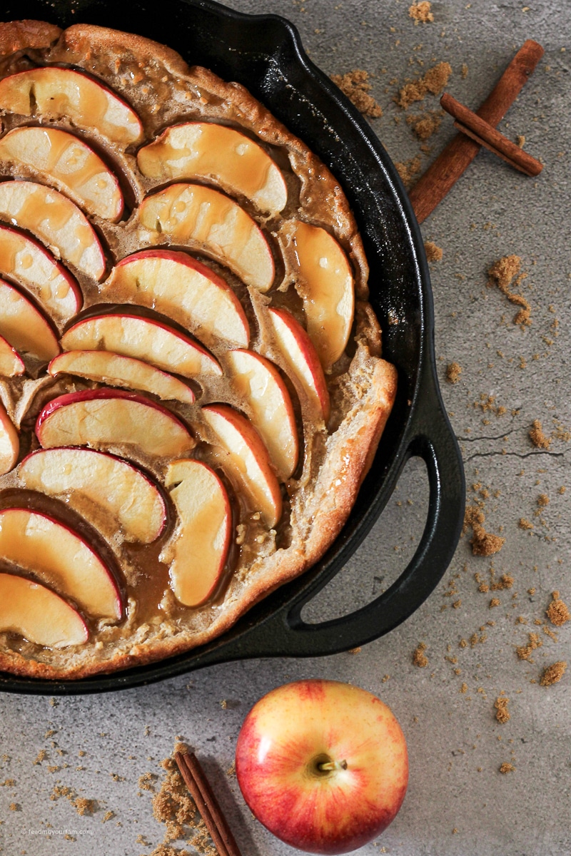 close up of a dutch baby pancake with apple slices in a cast iron skillet 