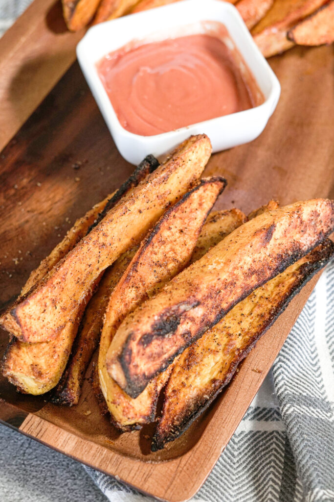 toasted sweet potatoes on a wooden serving platter with dipping sauce