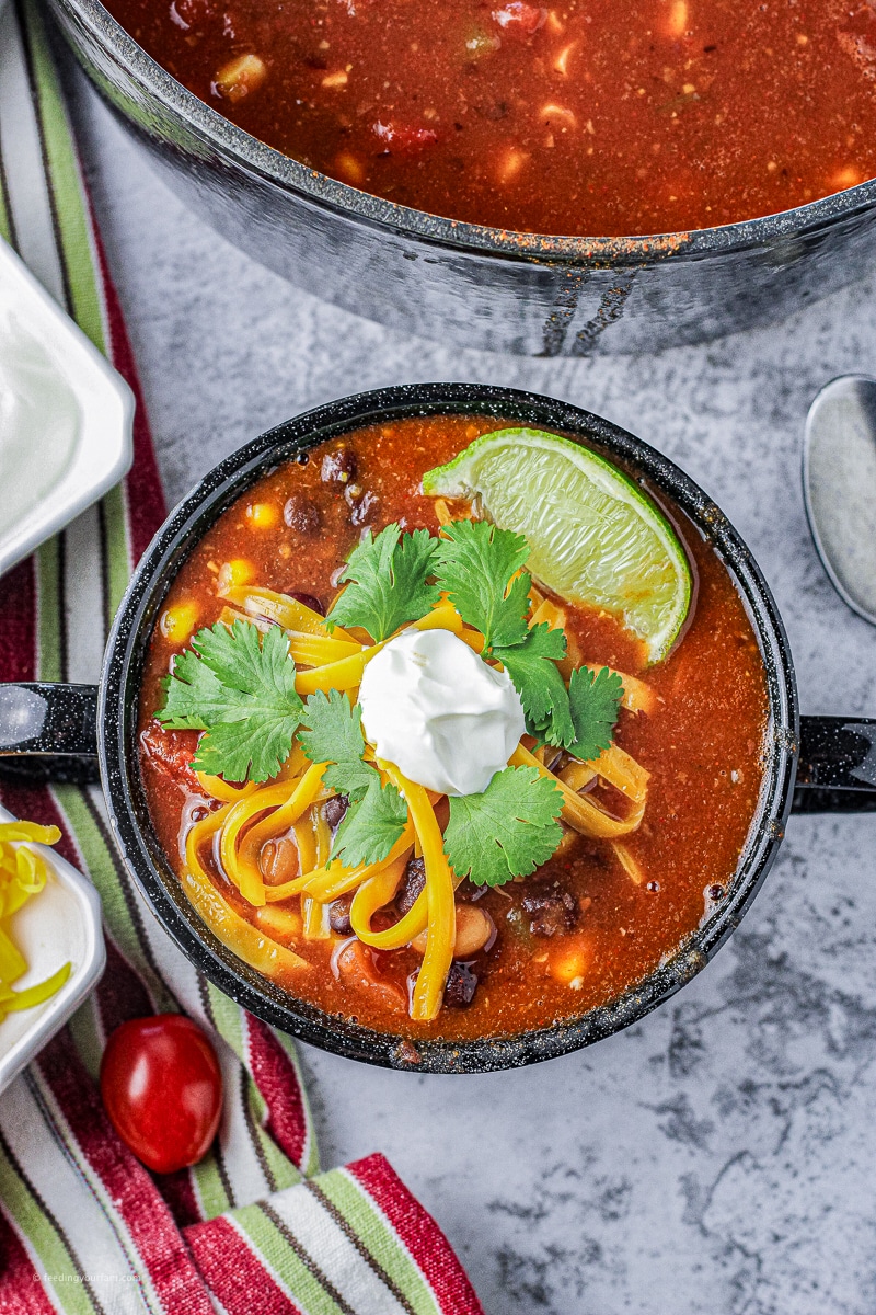 bowl of taco soup with beans and corn topped with sour cream, cheese, cilantro and limes