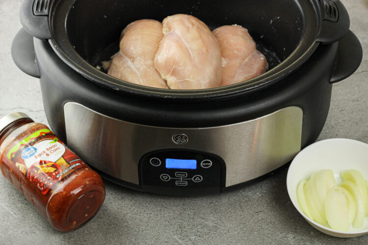 crockpot with chicken, salsa bottle and sliced onions