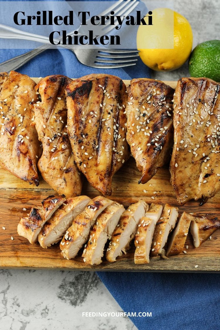 grilled chicken on a wooden cutting board. One chicken breast is sliced