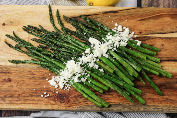 cooked asparagus on a wooden platter with feta cheese