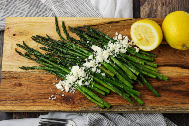 asparagus on wooden platter with lemons and feta