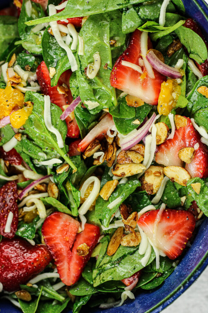 spinach, sliced strawberries, mandarin oranges, mozzarella cheese and toasted almonds in a blue salad bowl