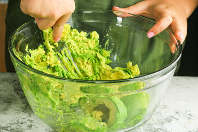 mashing avocado in a clear glass bowl