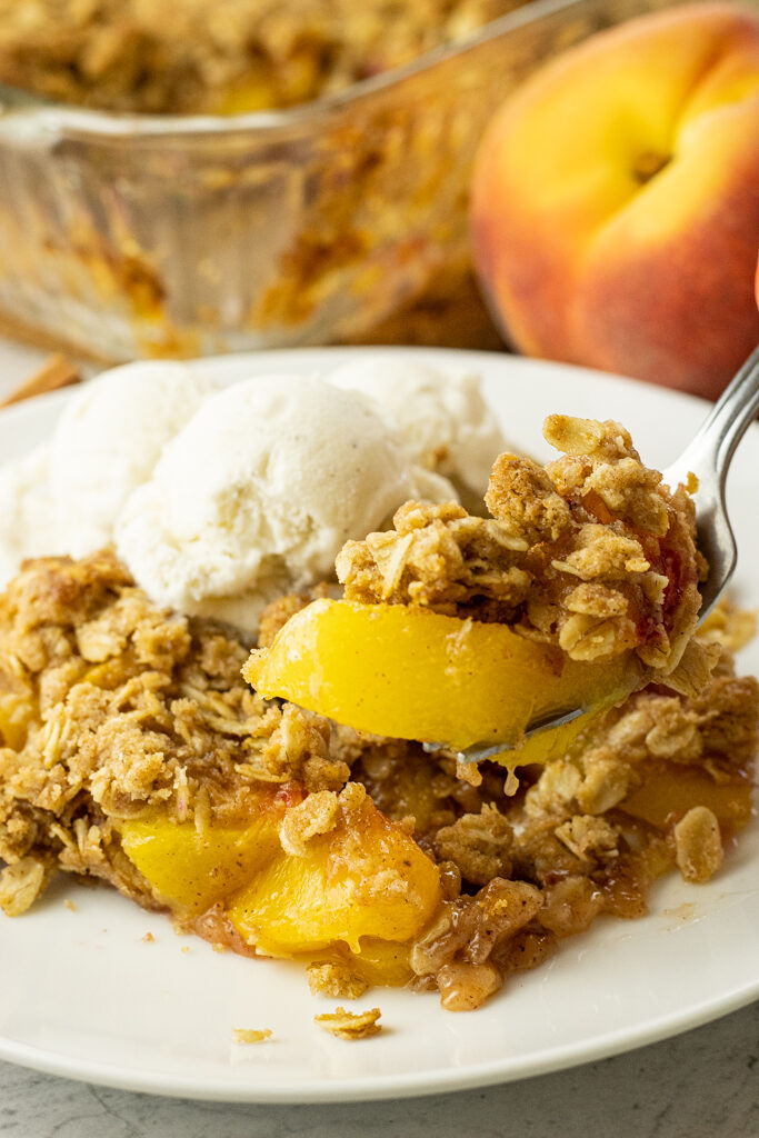fork lifting a scoop of peach crisp off a white plate