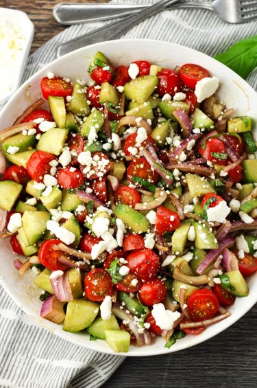cucumber tomato red onion salad with feta cheese in a white bowl