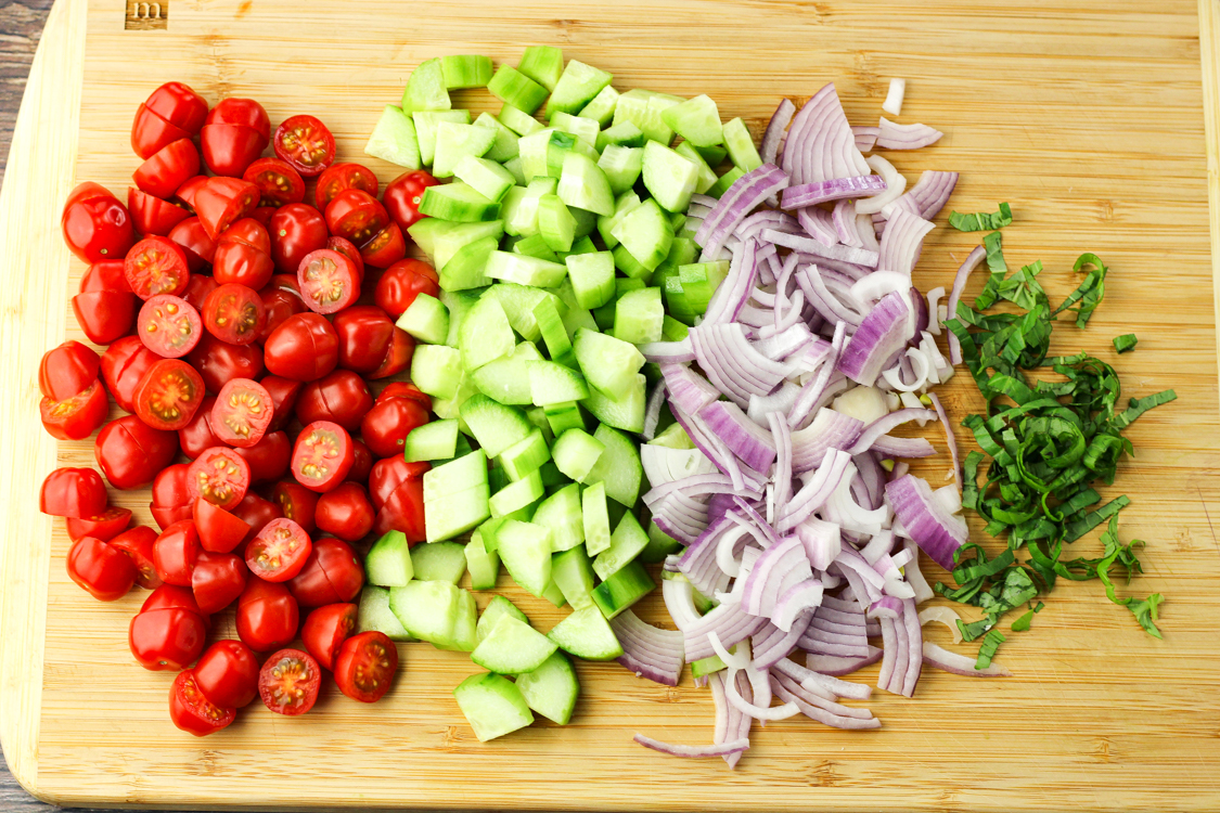 sliced tomatoes, cucumbers, red onions and basil on a wooden cutting board