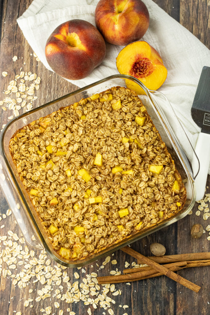 pan of baked oatmeal surrounded by dry oatmeal, peaches and cinnamon sticks