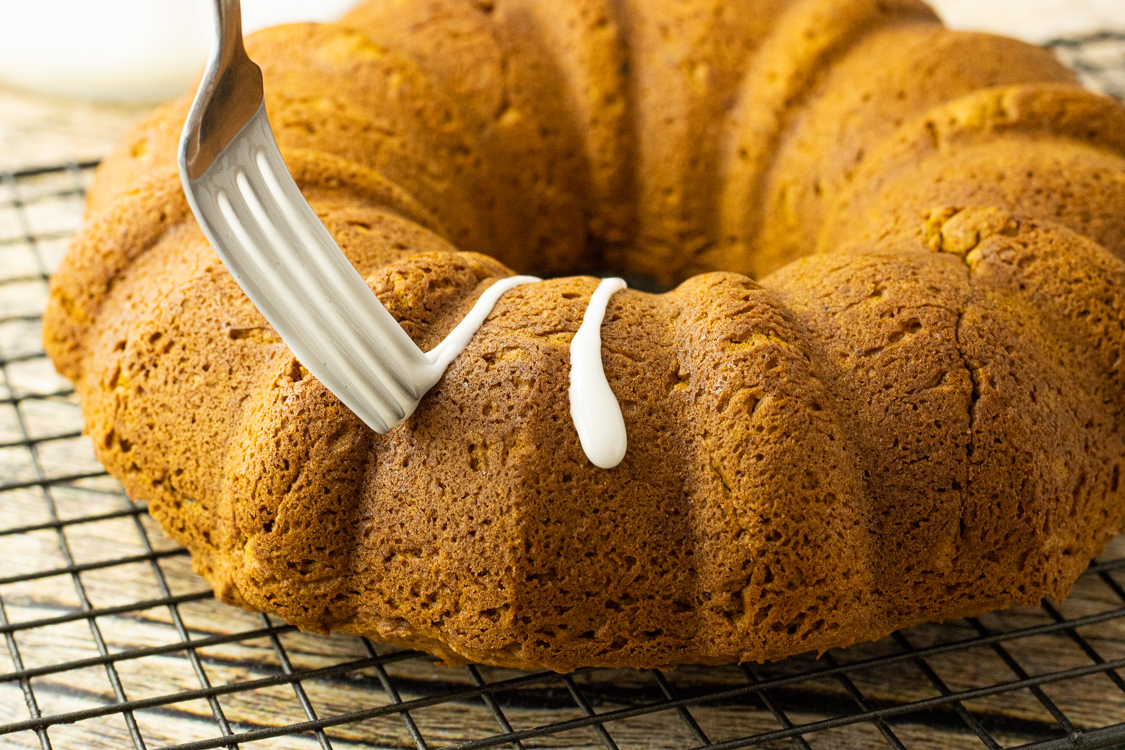 drizzling icing onto a pumpkin bundt cake with a fork