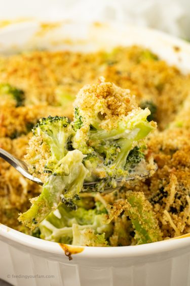 spoonful of creamy broccoli casserole from a white casserole dish