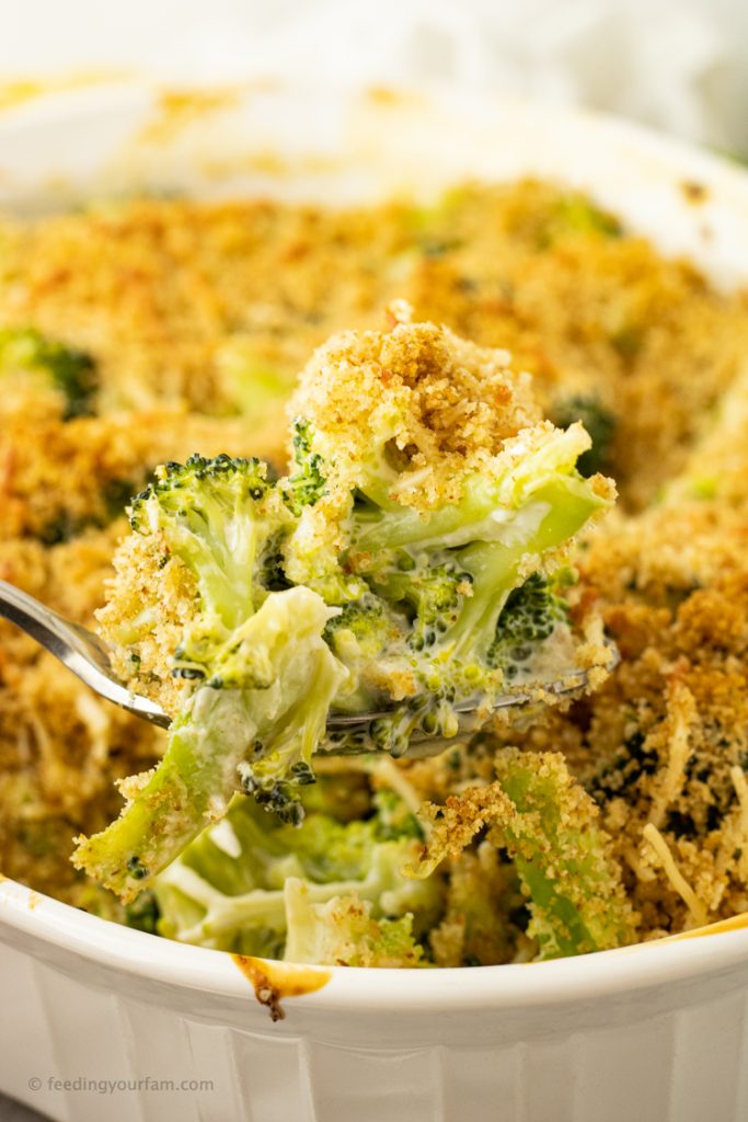 spoonful of creamy broccoli casserole from a white casserole dish