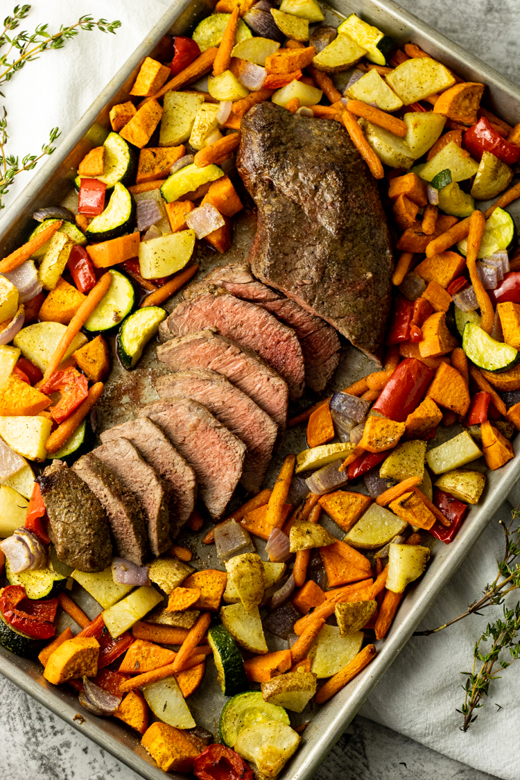 sliced steak surrounded by roasted vegetables on a sheet pan
