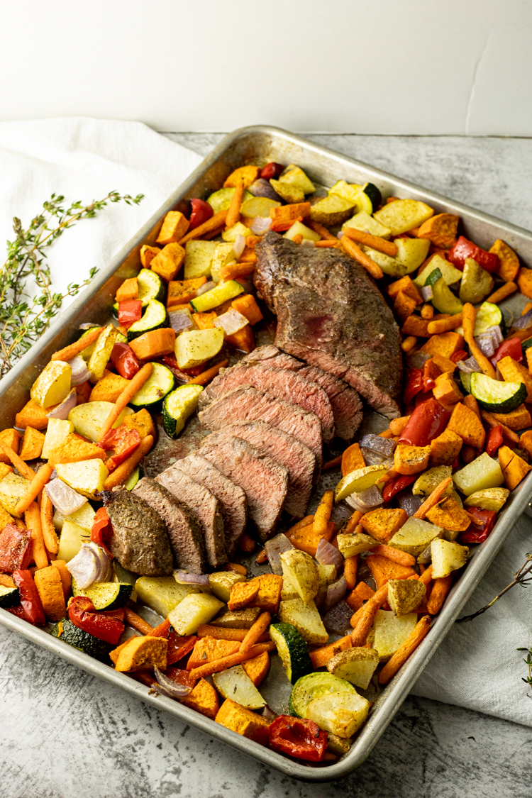 sliced roast in the center of vegetables on a sheet pan