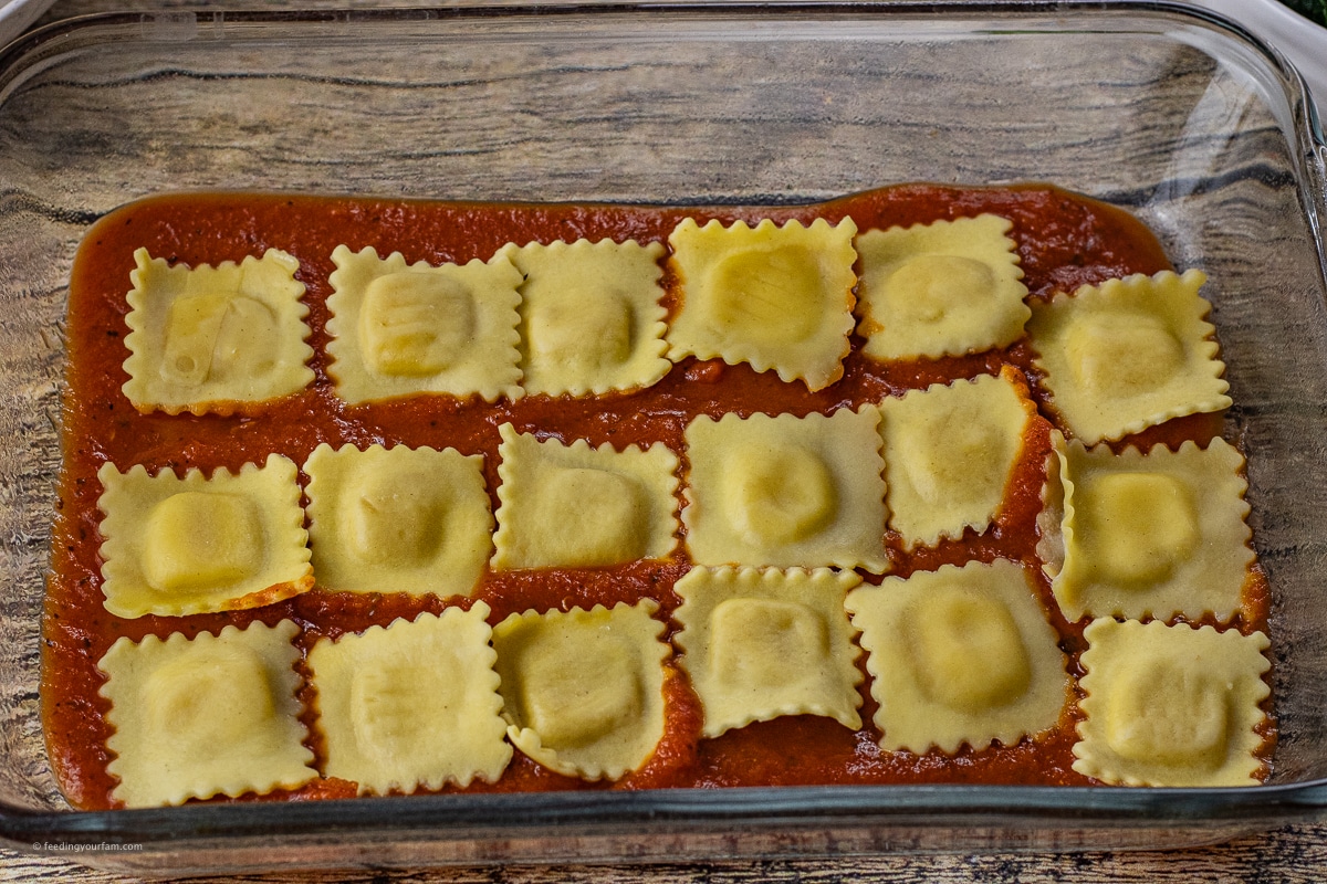 square cheese ravioli in a baking dish on a layer of spaghetti sauce to make ravioli lasagna