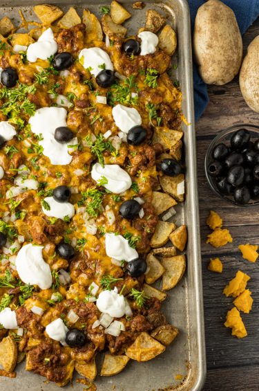 baking sheet of potato pieces topped with chili, sour cream and olives
