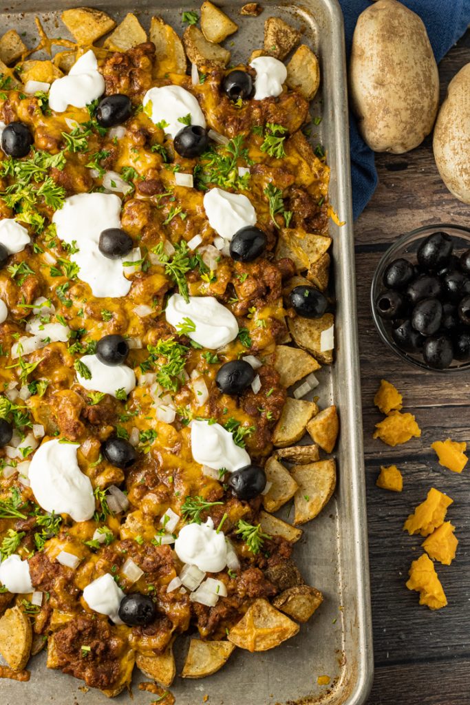 baking sheet of potato pieces topped with chili, sour cream and olives
