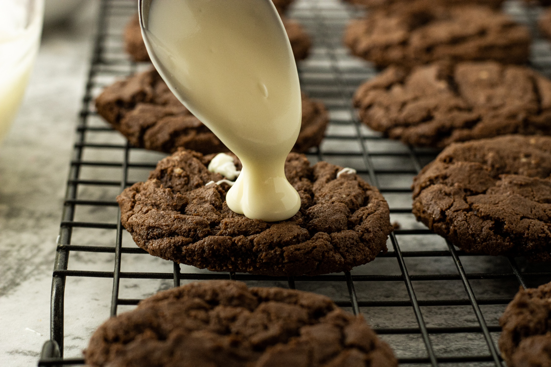 dripping melted white chocolate onto a chocolate cookie with a spoon