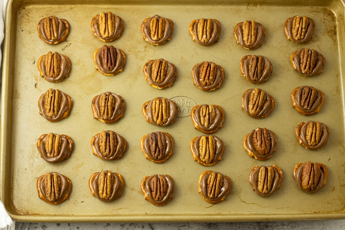 baking sheet full of Pretzels topped with melted Rolo candies and a pecan half