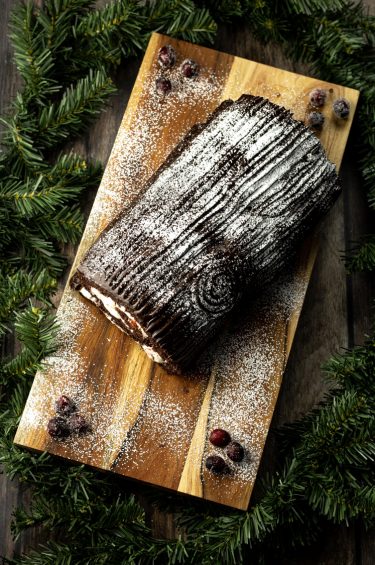 chocolate yule log cake on a wooden platter surrounded by evergreen pines