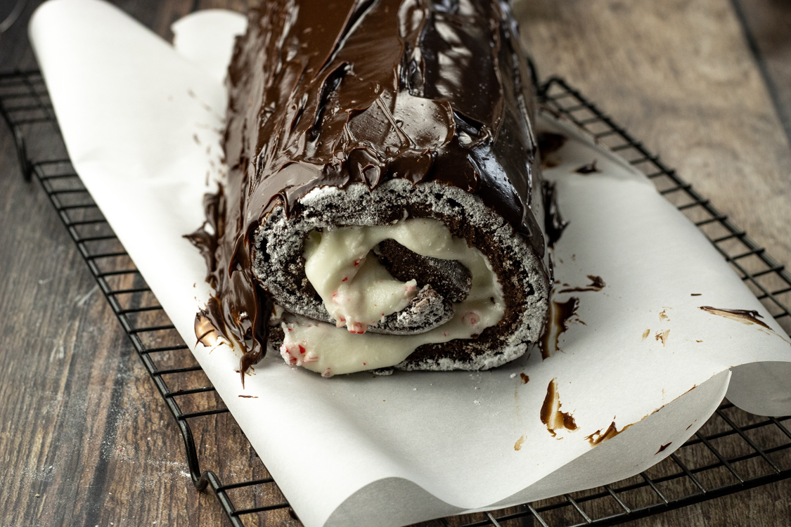 yule log on parchment paper being frosted with chocolate ganache