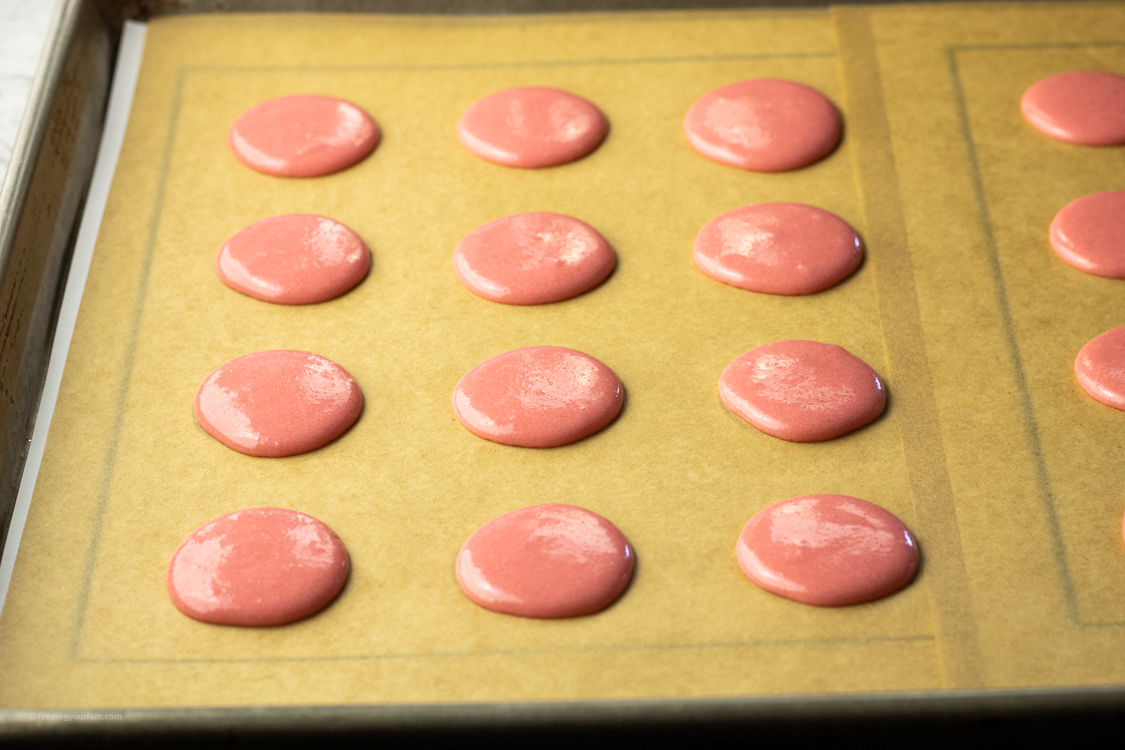 pink macaron batter on a parchment lined baking sheet