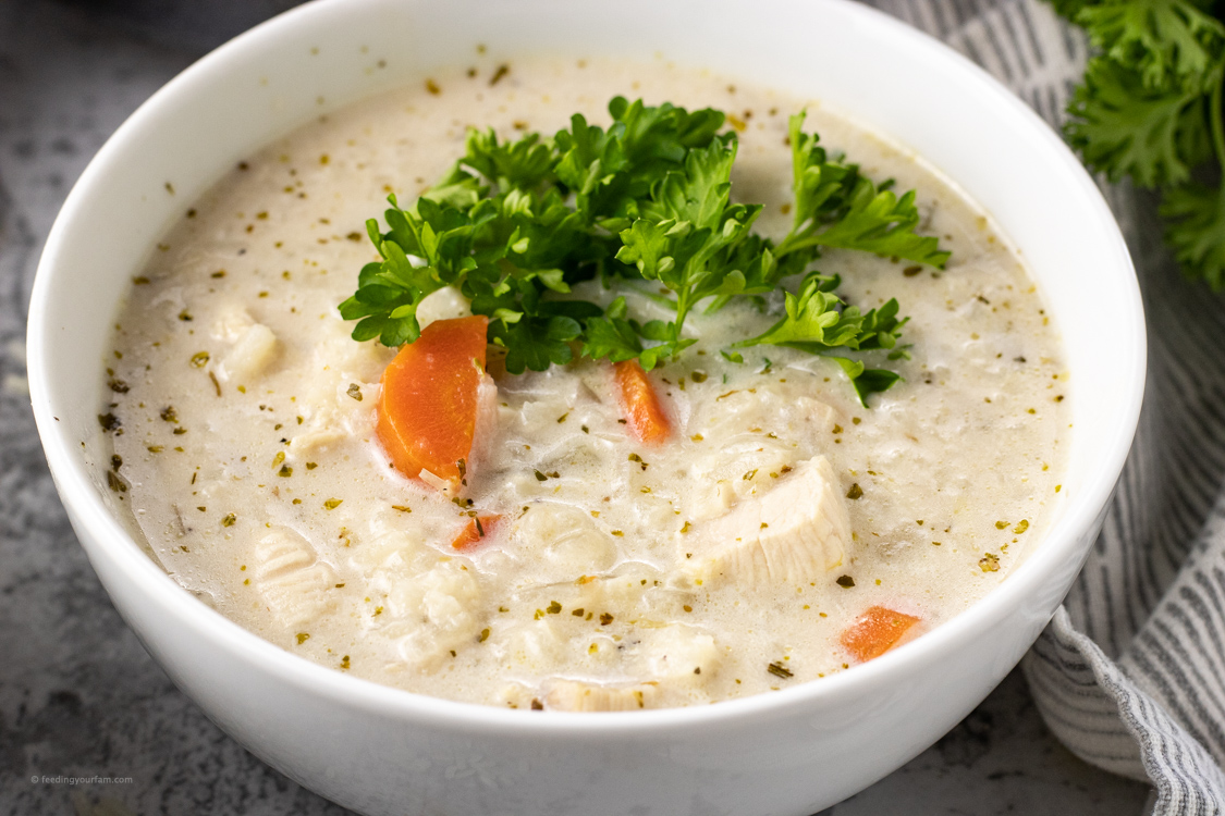 bowl of creamy soup with chicken and rice topped with fresh parsley