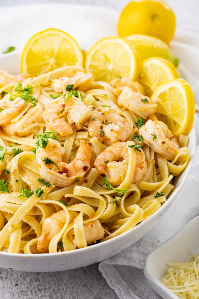 big white bowl of fettuccine noodles and shrimp with lemons