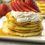 pile of pancakes topped with whipped cream and strawberries