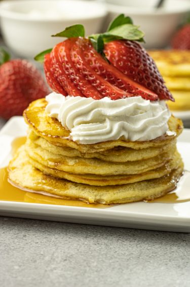 pile of pancakes topped with whipped cream and strawberries